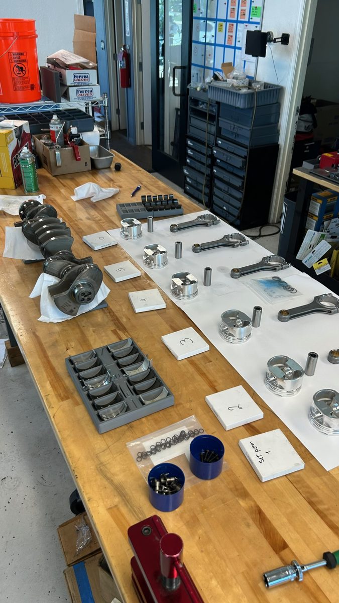 S58 rotating assembly laid out on the bench for measurement: crankshaft, forged rods, pistons and bearing shells each on labeled cards